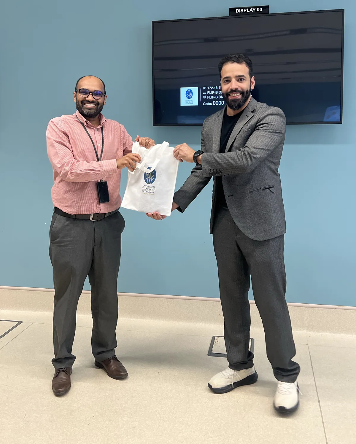 يوسف المالكي يحمل حقيبة هدية من جامعة بتروناس للتكنولوجيا مع أحد منسوبي الجامعة بعد المحاضرة